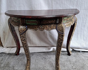 May include: A dark wood, half-moon console table with ornate carvings and curved legs. The table features gold, green, and blue accents along the apron and legs. The table's dimensions are approximately 36 inches wide and 18 inches deep.