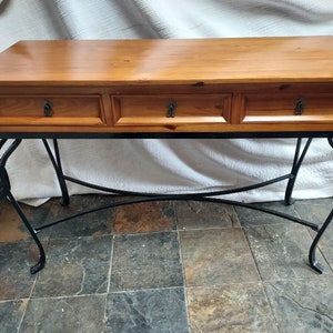 May include: A wooden console table with three drawers and black metal legs. The table has a light brown wood finish and the legs are curved.