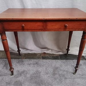 May include: A wooden table with two drawers and turned legs. The table has a light brown finish and is in good condition.