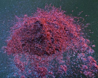 May include: A pile of iridescent red and blue glitter on a dark background.