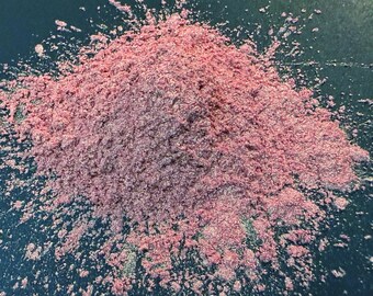 May include: A pile of pink and silver glitter pigment. The glitter is scattered on a dark blue surface.