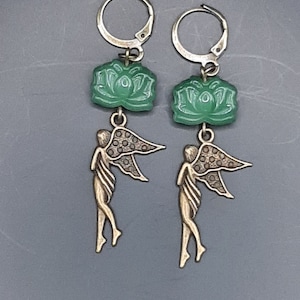 May include: A pair of earrings featuring a green jade lotus flower charm and a bronze fairy charm.