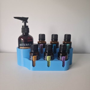 May include: A blue plastic organiser with seven slots holds various essential oil bottles. The bottles are labelled with the brand "dōTERRA" and names like "Wild Orange", "Clary Sage", and "Lemongrass".