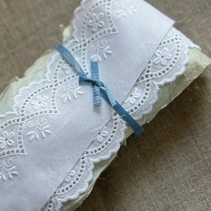 May include: White cotton lace trim with a scalloped edge and delicate floral embroidery. The lace is tied with a light blue ribbon.