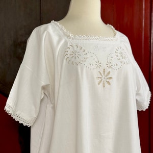 Puede incluir: Camisón blanco de algodón con ribete de encaje y un intrincado diseño floral recortado alrededor del escote.