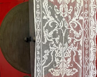 May include: White crocheted lace curtain with a floral pattern. The lace is hanging in front of a red door with a round, metal handle.