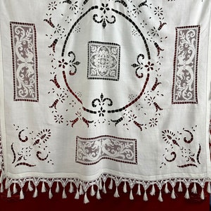 May include: White cotton tablecloth with intricate cut-out lace designs. The tablecloth has a square shape with a circular design in the center and a fringe border.