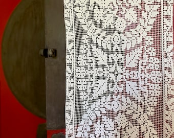 May include: White crocheted lace curtain with a geometric pattern. The lace is hanging in front of a red door.