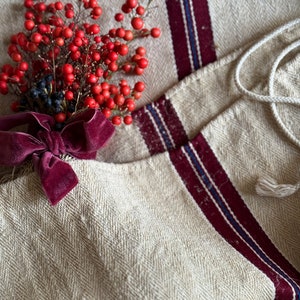 May include: A close-up of a beige linen fabric with red and blue stripes. A bouquet of red berries with a burgundy velvet ribbon is placed on the fabric.