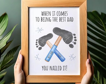 May include: A framed print with the text "When it comes to being the best dad, you nailed it!" features two gray footprints forming hammer heads. The hammers have blue handles with the words "Best Dad Ever."