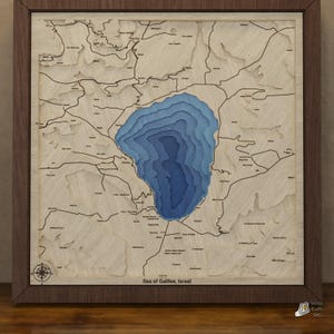 May include: A square wooden wall map of the Sea of Galilee, Israel, featuring layered light wood topography and a deep blue, multi-tiered lake center. The map includes black engraved place names, a compass rose, and the text Sea of Galilee, Israel.