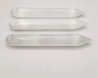 May include: Three white selenite wands with pointed ends. The wands are smooth and have a striated texture.