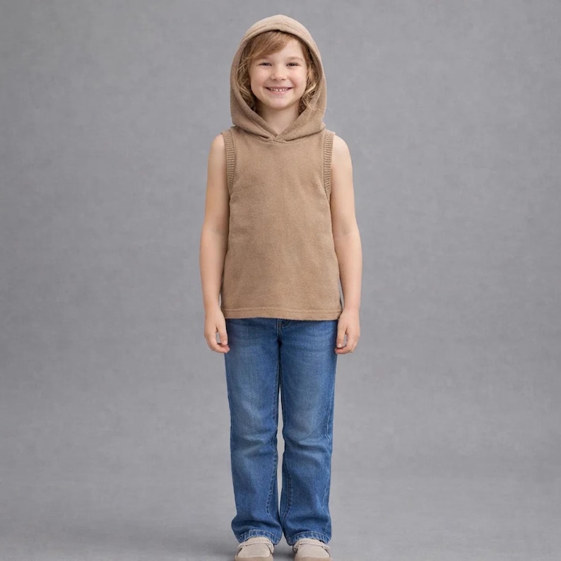 Op de afbeelding: Een kind draagt een mouwloze, gehoodie, bruin topje en een blauwe jeans. De top heeft geribbelde details op de schouders en een capuchon met trekkoord. De jeans is een klassieke blauwe denim wash.