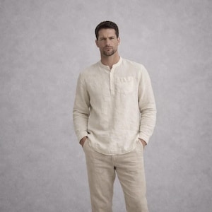 May include: A man wearing a beige linen shirt with a mandarin collar and a single chest pocket, paired with matching beige linen pants. The long-sleeved shirt is buttoned at the neck. The outfit is a neutral color.