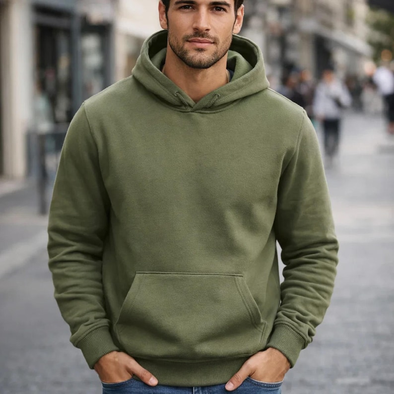 May include: Olive green hoodie with a kangaroo pocket and ribbed cuffs. The hooded sweatshirt is a casual garment, suitable for everyday wear. The long-sleeved top is made of a soft material.