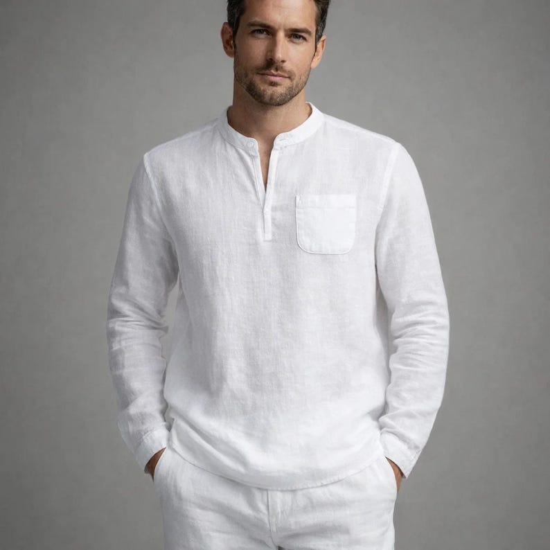 May include: White long-sleeve linen shirt with a mandarin collar and a chest pocket. The shirt has a button-down placket and is paired with white pants. The outfit is made of a lightweight, breathable fabric, perfect for warm weather.