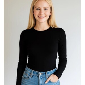 May include: A black long-sleeve shirt with a crew neck. The shirt is paired with blue jeans. The model is smiling, with blonde hair.