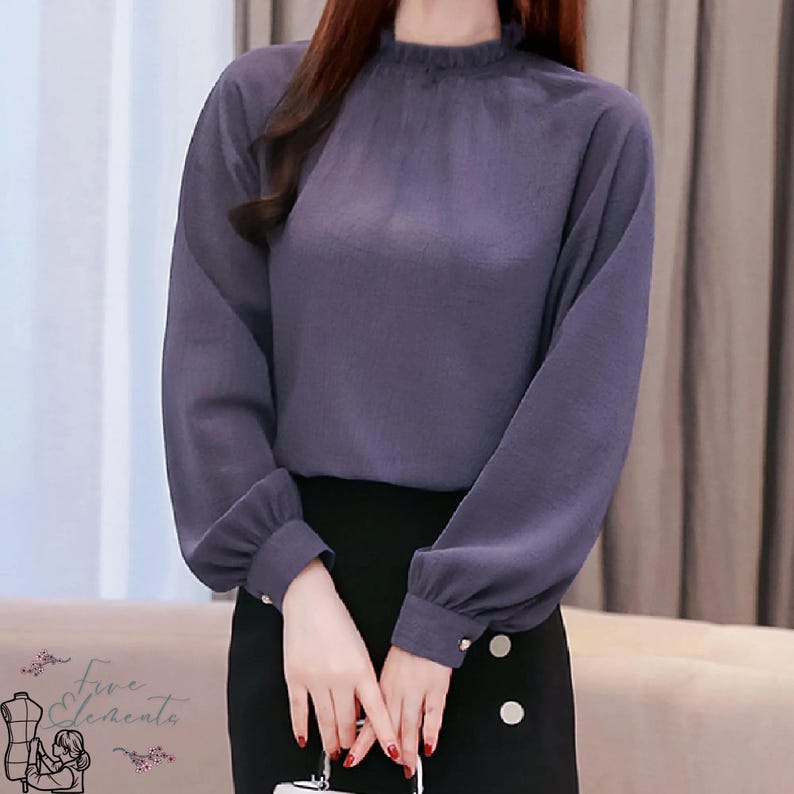 May include: A long-sleeved, periwinkle blouse with a high, ruffled neckline and buttoned cuffs. The blouse is paired with a black skirt. The image features the "Five Elements" logo in the lower left corner.