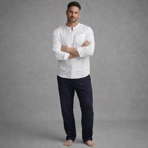 May include: A white long-sleeve shirt with a mandarin collar and a chest pocket, paired with navy blue pants. The outfit is simple and classic, suitable for casual wear. The model is standing with arms crossed.