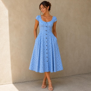 Pode incluir: Um vestido midi azul claro com decote redondo, mangas curtas e uma saia plissada e rodada. O vestido &eacute; adornado com um pequeno padr&atilde;o floral azul escuro repetitivo e possui uma fila vertical central de bot&otilde;es na parte da frente.