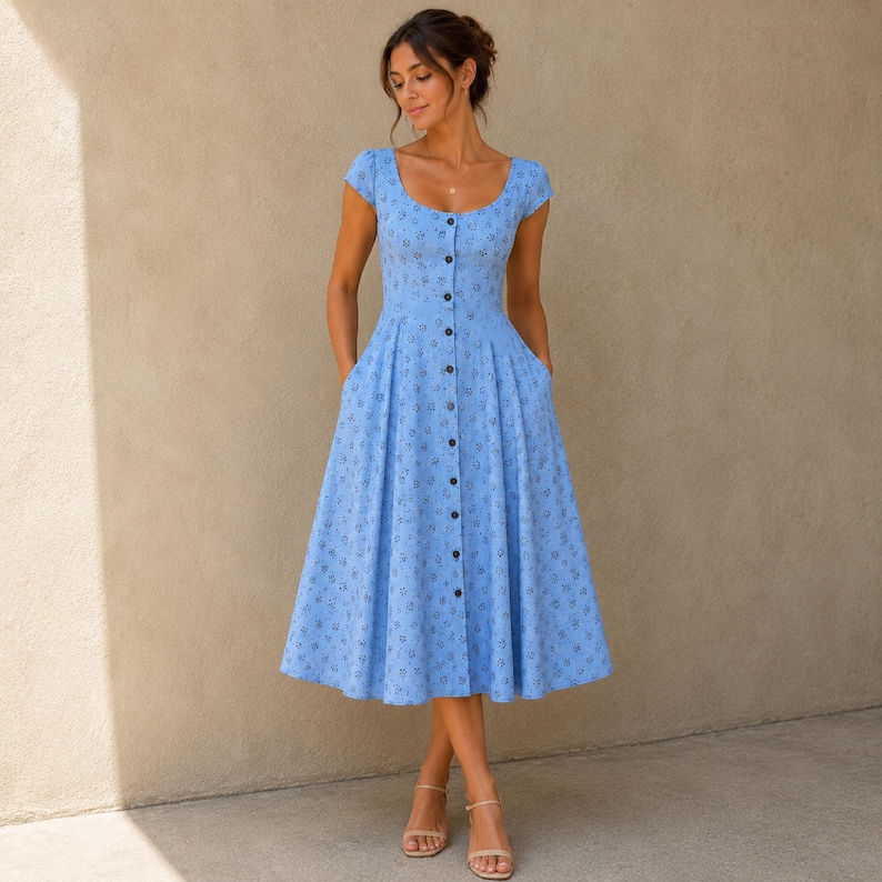 Pode incluir: Um vestido midi azul claro com decote redondo, mangas curtas e uma saia plissada e rodada. O vestido &eacute; adornado com um pequeno padr&atilde;o floral azul escuro repetitivo e possui uma fila vertical central de bot&otilde;es na parte da frente.