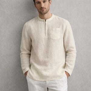 May include: A cream-colored long-sleeve shirt with a mandarin collar and a quarter-zip closure. The shirt has a single chest pocket and is made of a lightweight, textured fabric. The model is wearing white pants.