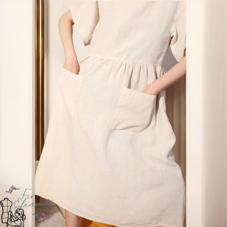 Puede incluir: Un vestido sencillo de lino de color blanco roto con mangas cortas y dos bolsillos de parche. El vestido tiene una cintura fruncida y una falda fluida.