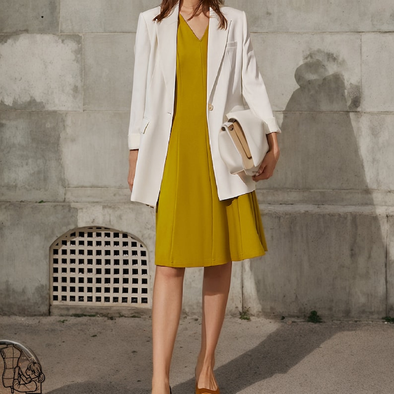 May include: A woman wearing a white blazer over a mustard yellow dress and a white handbag.
