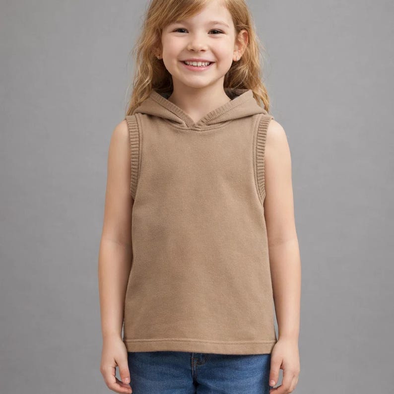 Op de afbeelding: Een mouwloze, bruine hoodie met een capuchon met trekkoord en geribde boorden. Het kledingstuk is gemaakt van een zacht materiaal en is ontworpen voor kinderen. De achtergrond is effen grijs.