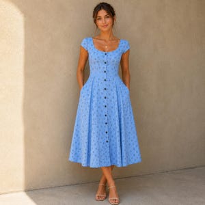 Pode incluir: Um vestido midi azul claro com decote redondo, mangas curtas e saia ampla. O vestido &eacute; adornado com um pequeno padr&atilde;o floral azul escuro repetitivo e tem uma fila vertical de bot&otilde;es escuros ao longo do centro da parte frontal.