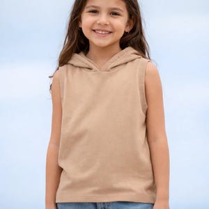 Op de afbeelding: Een mouwloze, bruinachtige hoodie met een capuchon met trekkoord. De hoodie heeft geribbelde details langs de armsgaten en capuchon. De achtergrond is een lichtblauwe lucht. De hoodie is gemaakt van een zacht, comfortabel materiaal.