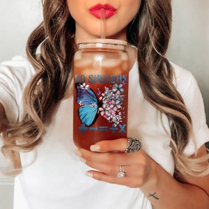 May include: A clear glass reusable water bottle with a bamboo lid and a colorful butterfly design. The bottle has the text "Ed Sheeran" and "+" "=" "x" printed on it.