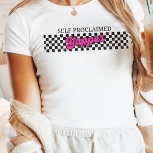 May include: White t-shirt with a black and white checkered pattern and the text "SELF PROCLAIMED Yapper" in pink letters.