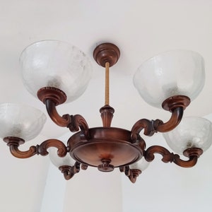 May include: A wooden chandelier with five clear glass shades. The chandelier has a brown wood finish and intricate carvings.