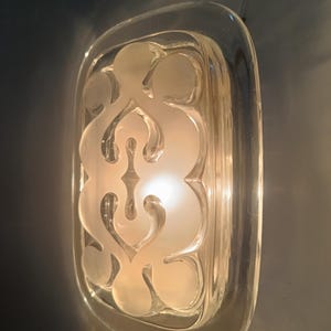 May include: A clear glass butter dish with a frosted design of a stylized floral pattern. The dish is rectangular and has a rounded edge.