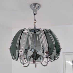 Könnte beinhalten: Ein Chrom- und Rauchglas-Kronleuchter mit sechs Lichtern. Der Kronleuchter hat ein geometrisches Design mit runder Form.