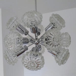 May include: A vintage chandelier with a chrome finish and multiple clear, faceted glass shades. The light fixture is suspended from the ceiling and features a central hub with radiating arms holding the shades.