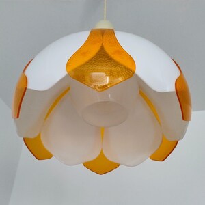 Peut inclure: Un luminaire suspendu blanc et orange. La lampe a un design en forme de fleur avec des p&eacute;tales blancs et des accents orange. Les sections orange ont un aspect textur&eacute; et mouchet&eacute;. La lampe est suspendue &agrave; un cordon blanc.