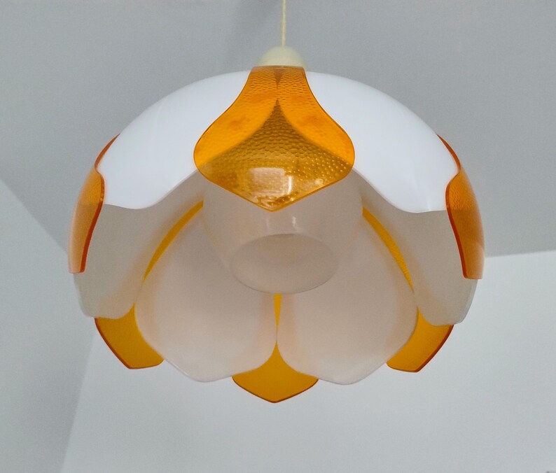 Peut inclure: Un luminaire suspendu blanc et orange. La lampe a un design en forme de fleur avec des p&eacute;tales blancs et des accents orange. Les sections orange ont un aspect textur&eacute; et mouchet&eacute;. La lampe est suspendue &agrave; un cordon blanc.