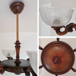 May include: A wooden chandelier with five frosted glass shades. The chandelier has a brown wooden frame with intricate carvings and a rope-like cord hanging from the center.