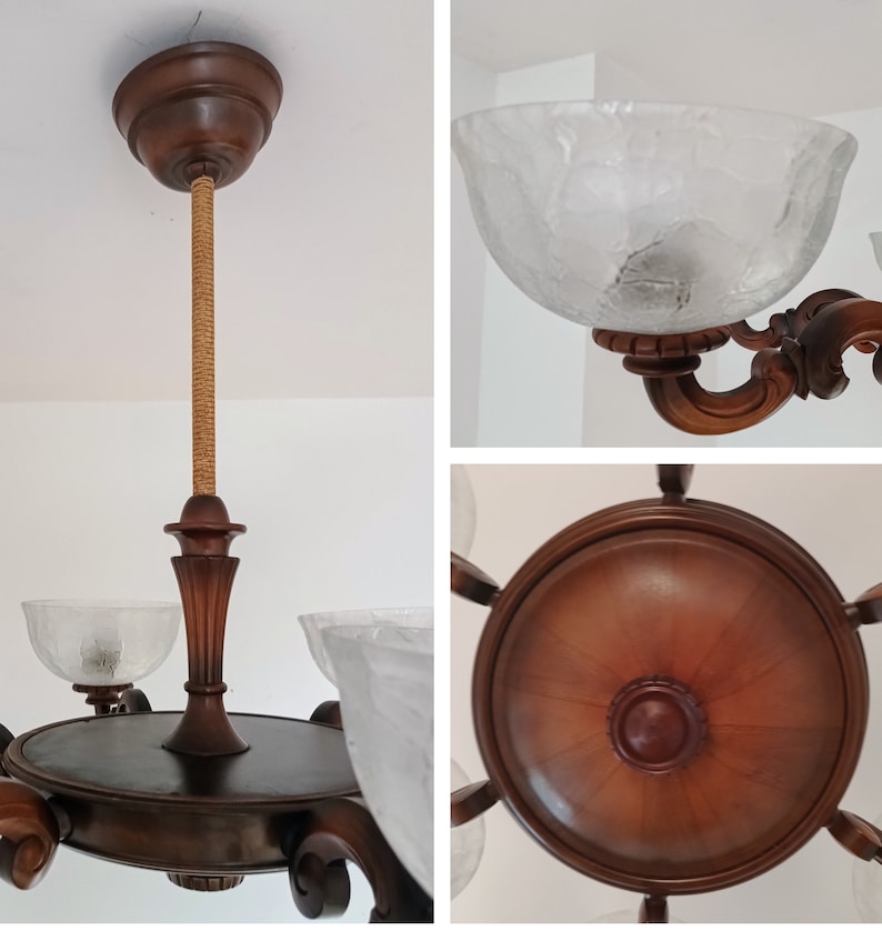 May include: A wooden chandelier with five frosted glass shades. The chandelier has a brown wooden frame with intricate carvings and a rope-like cord hanging from the center.