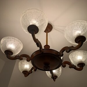 May include: A six-light chandelier with a dark wood frame and clear glass shades. The shades have a textured, crackled glass design.