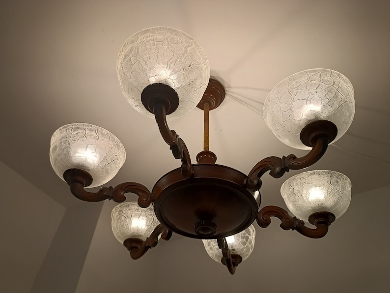 May include: A six-light chandelier with a dark wood frame and clear glass shades. The shades have a textured, crackled glass design.