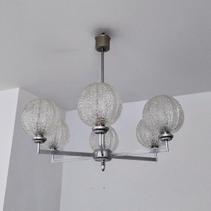 Könnte beinhalten: Ein Vintage-Kronleuchter mit fünf transparenten, strukturierten Glaskugelschirmen. Die Leuchte hat ein silberfarbenes Metallgestell und einen zentralen Stiel zur Deckenmontage. Die Kugeln sind gleichmäßig verteilt.