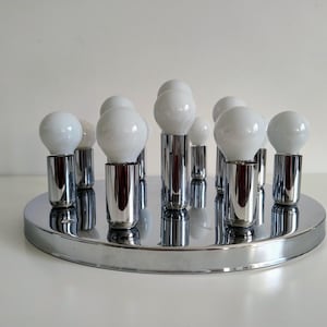 May include: A chrome ceiling light fixture with 10 white light bulbs. The fixture has a round base and the bulbs are arranged in a circular pattern.