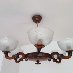 May include: A wooden chandelier with four frosted glass shades. The chandelier has a brown finish and ornate details.
