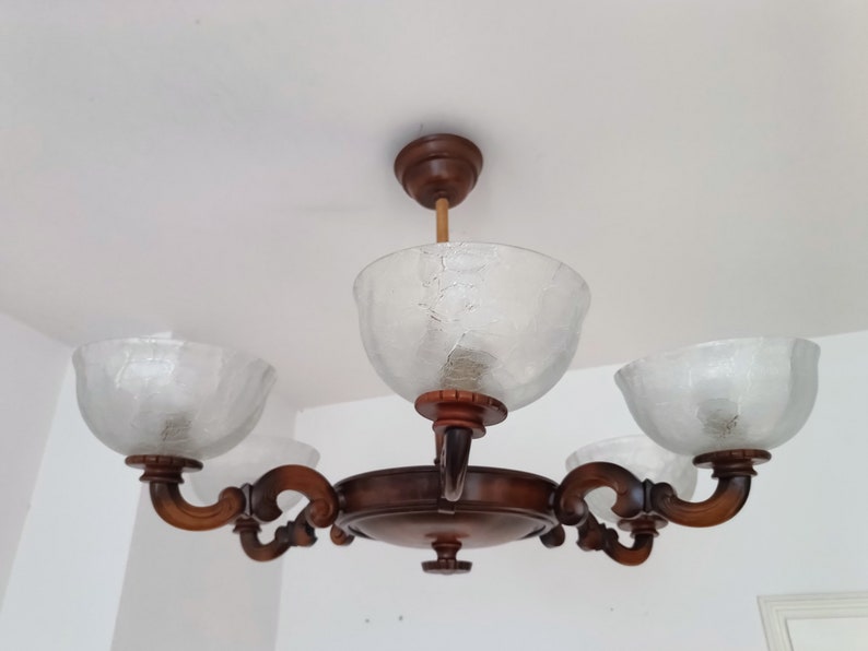 May include: A wooden chandelier with four frosted glass shades. The chandelier has a brown finish and ornate details.