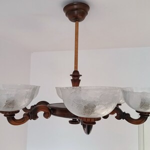 May include: A wooden chandelier with four frosted glass shades. The chandelier has a brown wooden frame and a rope-like cord.