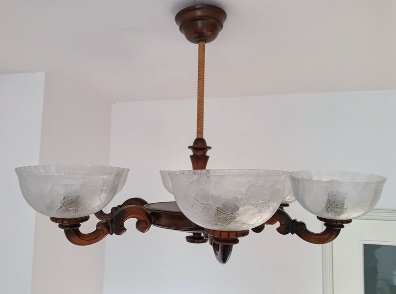May include: A wooden chandelier with four frosted glass shades. The chandelier has a brown wooden frame and a rope-like cord.