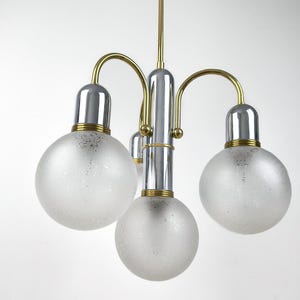 Könnte beinhalten: Ein Vintage-Kronleuchter mit einer zentralen Chromsäule und vier Kugelschirmen aus mattiertem Glas. Die Leuchte hat goldfarbene gebogene Arme und eine Messingstange zum Aufhängen. Das Design ist modern.